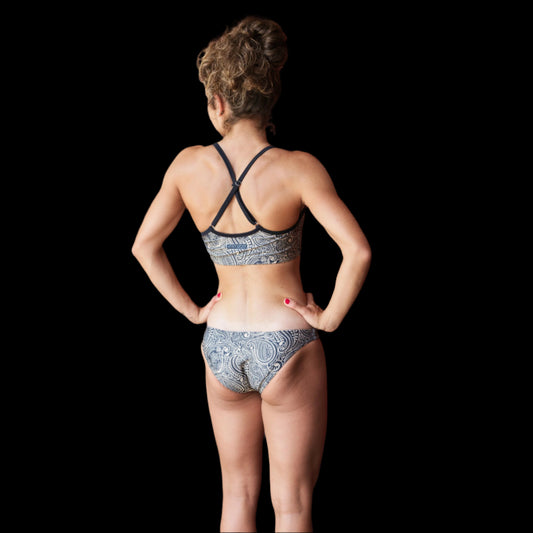Woman wearing a patterned Pasley bikini standing on a wooden deck with a red wall in the background.