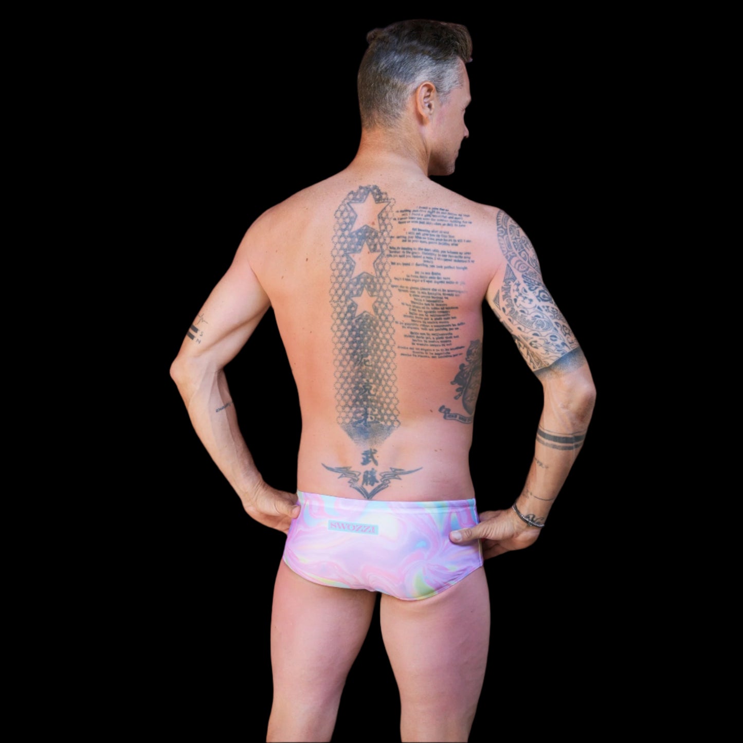 Fit man wearing pink swirl pattern one piece swimwear with a brand logo hands on hips