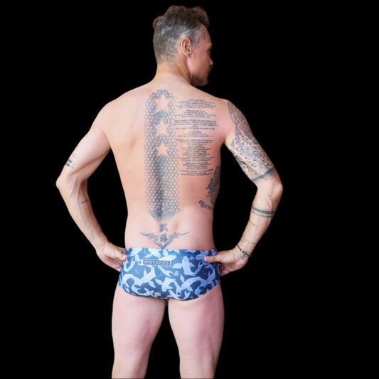 Fit man wearing Blue Koi Fish pattern one piece swimwear with a brand logo hands on hips