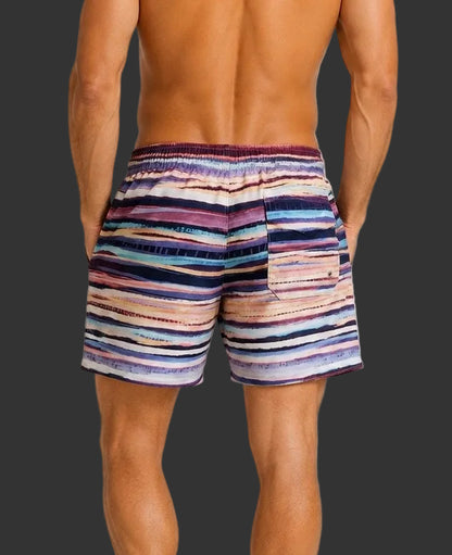 A man viewed from the back wearing striped swim trunks with horizontal bands of purple, blue, pink, beige, and white on a light gray studio background.