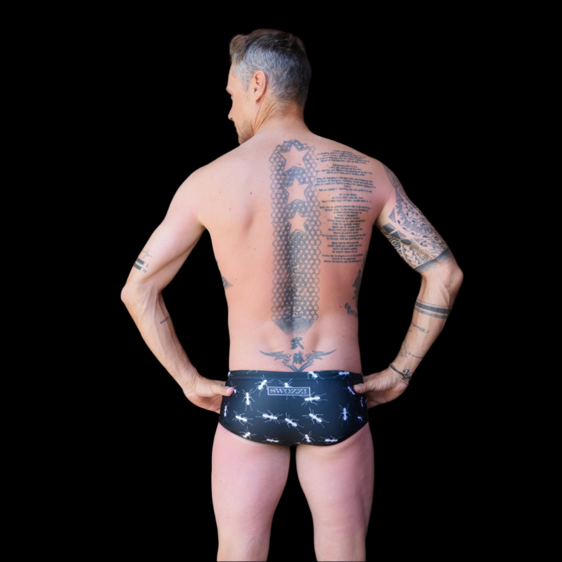 Fit man wearing black with white ants pattern one piece swimwear with a brand logo  hands on hips