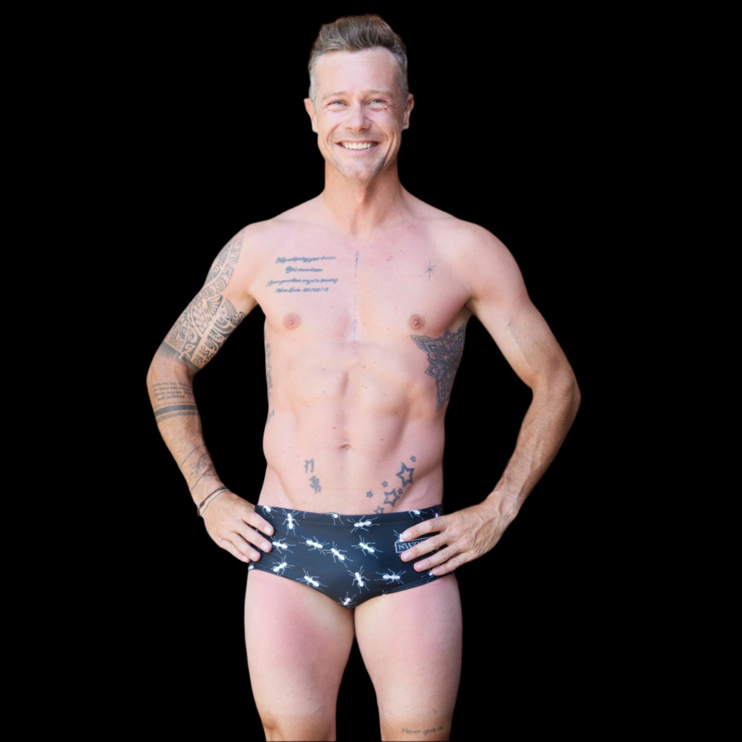 Fit man wearing black with white ants pattern one piece swimwear with a brand logo  hands on hips