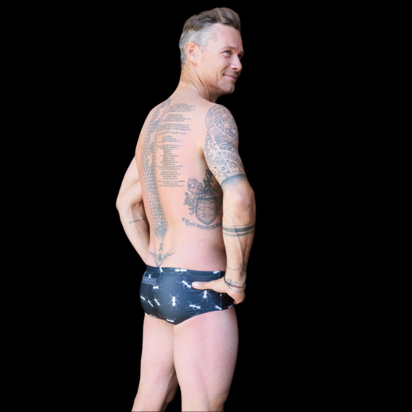 Fit man wearing black with white ants pattern one piece swimwear with a brand logo  hands on hips