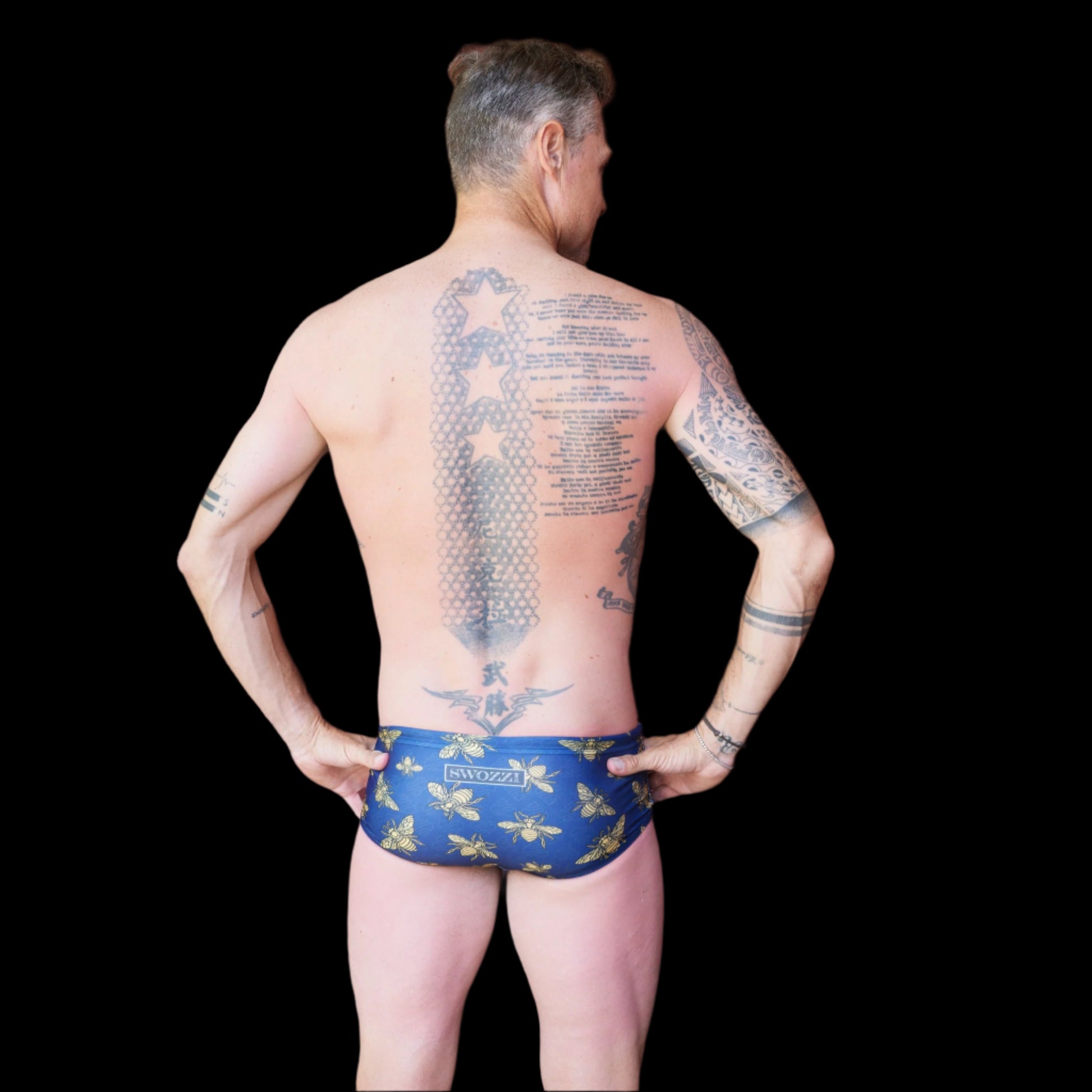 Fit man wearing Blue and gold bees pattern one piece swimwear with a brand logo  hands on hips
