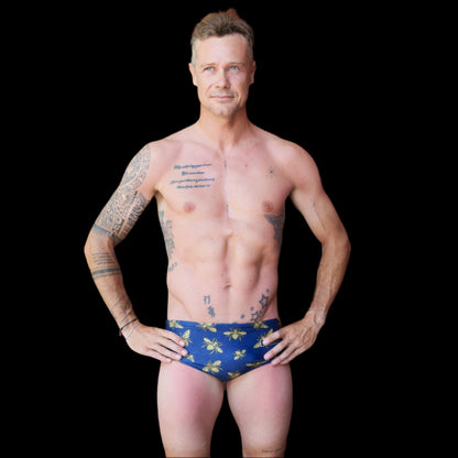 Fit man wearing Blue and gold bees pattern one piece swimwear with a brand logo  hands on hips