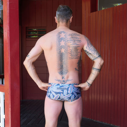 Fit man wearing Colourful Feathers pattern one piece swimwear with a brand logo  hands on hips