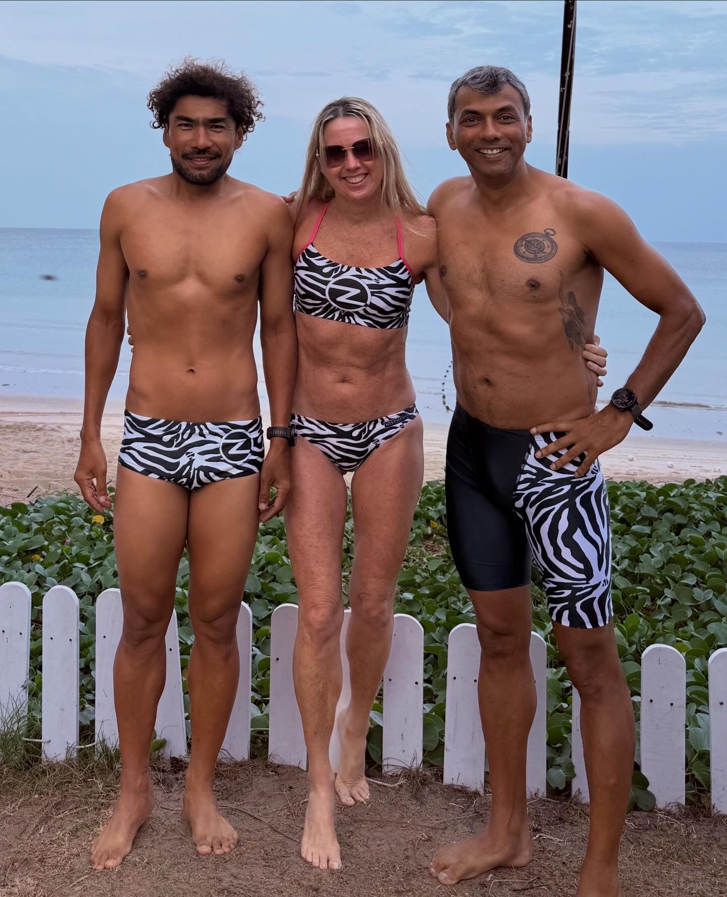 Three people in zebra-striped swimwear standing on a beach in Phuket. Z-Coaching Athletes